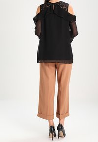 Blusa nera con dettagli in pizzo e maniche con volant, abbinata a pantaloni ampi beige chiaro e scarpe con tacco nere.