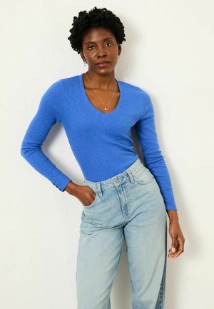 Blue long-sleeve V-neck top in a textured, lightweight material paired with light-wash high-waisted jeans.