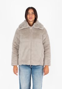 Giacca in pelliccia sintetica grigia con colletto ampio e chiusura con zip, caratterizzata da una consistenza morbida e una vestibilità leggermente più ampia, abbinata a jeans blu.