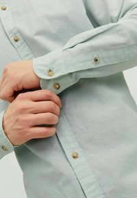 Lichtgroen button-up shirt van een zachte stof. Voorzien van bruine knopen en een relaxte pasvorm met opgerolde mouwen.