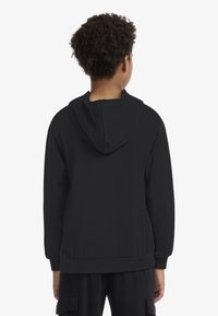 Hanorac negru cu glugă, cu textură netedă, manșete și tiv striate. Are o cusătură centrală pe spate și un croi lejer.