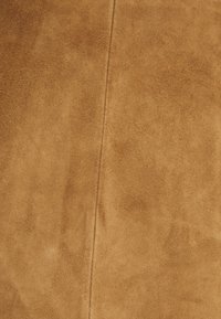 Tissu en daim de couleur tan chaud avec une texture lisse. Présente un motif de grain subtil et une couture centrale verticale.