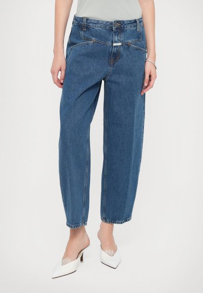Jean en denim bleu avec une coupe ample, taille haute et jambe fuselée. Détails de broderie notables et quincaillerie contrastante à la taille.