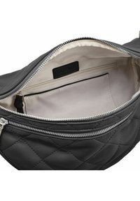 Interno di borsa in pelle trapuntata nera con fodera beige, dotata di tasca con zip ed etichetta. Texture liscia e dettagli in metallo argentato.