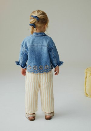 Jeansjacke mit floraler Stickerei am Saum, kombiniert mit cremefarbenen und gelb gestreiften Hosen sowie Sandalen im Animalprint.