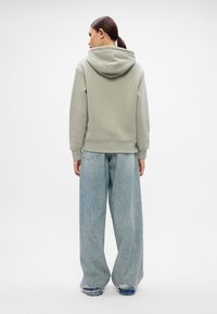 Lys grå hettegenser med forlomma og snor i hetta, kombinert med løstsittende lyseblå jeans med slitte detaljer.