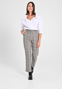 Weißes Hemd mit übergroßem Kragen; graue Karohose mit hohem Bund; schwarze Slipper mit goldfarbener Kettendetail; glatte Stoffoberfläche.