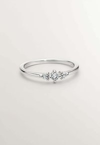 Anillo de plata con tres pequeñas piedras redondas y transparentes, colocadas en el centro. Banda lisa con un acabado pulido, diseño minimalista.