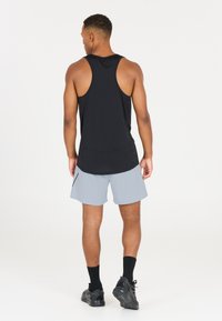 Schwarzes ärmelloses Sporttop mit abgerundetem Saum, kombiniert mit hellgrauen Shorts. Verfügt über eine Rückentasche und schwarze Sportschuhe.