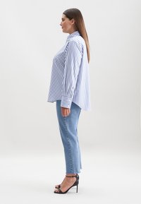 Gestreiftes blau-weißes Langarmhemd, entspannte Passform, kombiniert mit hellblauen, hochgeschnittenen Jeans und schwarzen Absatzsandalen.