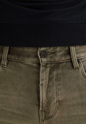 Nahaufnahme von olivgrünen Jeans aus Denim mit Knopf- und Reißverschluss, Gürtelschlaufen, kombiniert mit einem Kleidungsstück mit schwarzem, geripptem Saum.