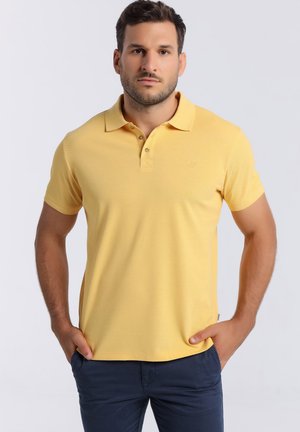 Polo amarillo hecho de una tela texturizada con un patrón sutil, tapeta de tres botones y pequeño logo en el pecho.