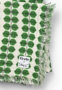 Bomulds tørklæde med et grønt blade mønster på en cremefarvet baggrund, med frynser i kanten. Etiketten siger "Elodie x StigL."