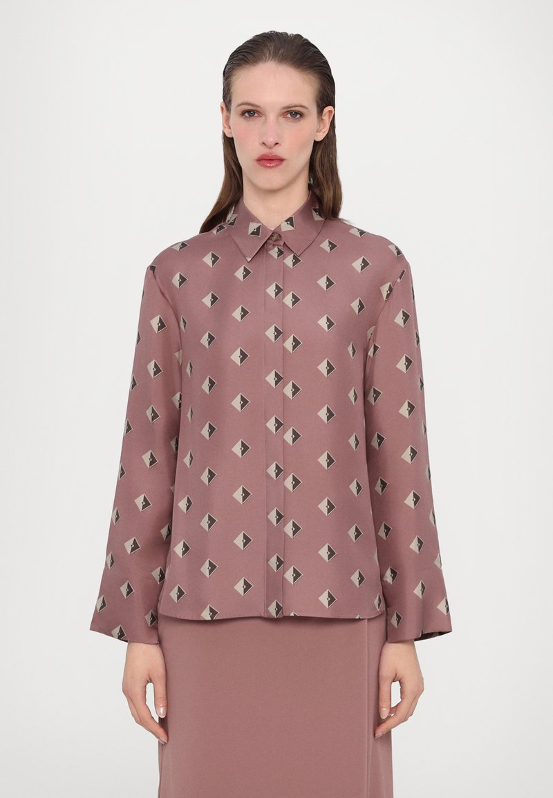 Langermet bluse i rosafarget stoff med et geometrisk mønster i svart og beige, med klassisk krage og knappelukking foran.