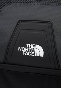 Black fabric backpack with a textured finish and a prominent white logo featuring "THE NORTH FACE" on a black rubber patch.
