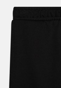 Čierne joggingové nohavice vyrobené z mäkkého, elastického materiálu s elastickým pásom a hladkou textúrou. Jednoduchý dizajn bez vzorov alebo akcentov.