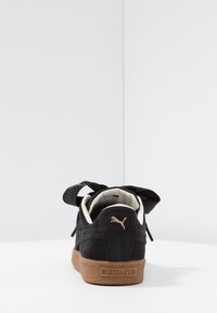 Černé kordové tenisky s texturovaným svrškem, s růžovým logem a hnědou gumovou podrážkou. Obsahují dlouhé černé tkaničky uvázané na zadní straně.