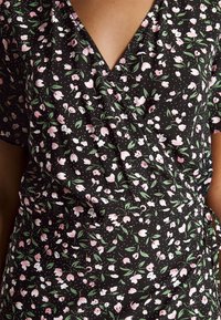 Robe en tissu noir avec un petit motif floral rose et blanc, décolleté en V, manches courtes et taille froncée avec lien.