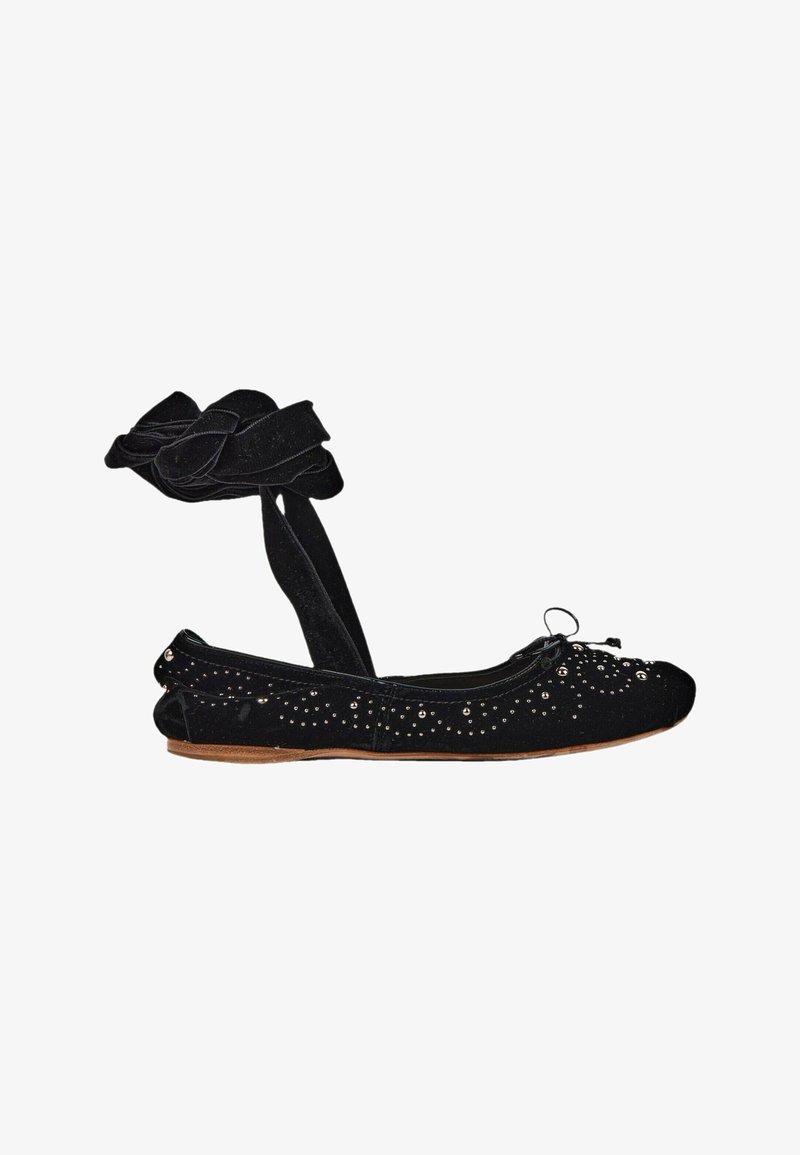 Ballerine noire avec lien à nouer à la cheville et petits clous argentés décorant la tige en tissu et une semelle plate couleur beige.