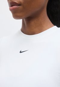 Κοντινό πλάνο του λαιμού και των χειλιών ενός ατόμου που φοράει λευκό πουκάμισο με ένα μικρό μαύρο λογότυπο Nike κάτω από το γιακά.