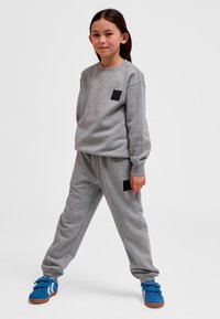 Grijze set bestaande uit een sweatshirt en joggingbroek met zwarte stoffen inzetstukken. Model draagt blauwe klittenbandsneakers. Zachte textuur, casual ontwerp.