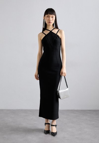 Abito nero aderente con texture a costine, scollo halter e spalline incrociate. Abbinato a una borsa metallizzata argento e tacchi neri.