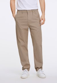 Beige broek van lichtgewicht stof, met een rechte pijp en plooien, gecombineerd met witte sneakers.