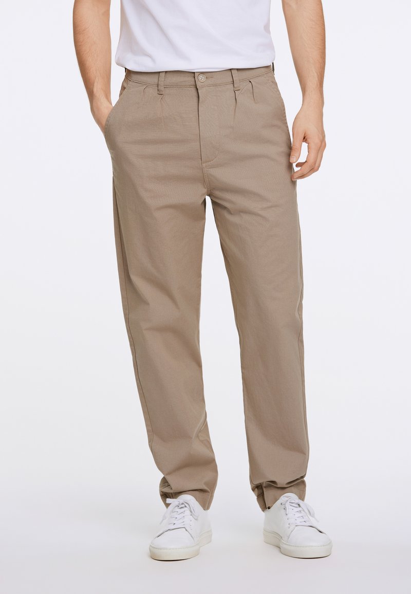 Beige broek van lichtgewicht stof, met een rechte pijp en plooien, gecombineerd met witte sneakers.