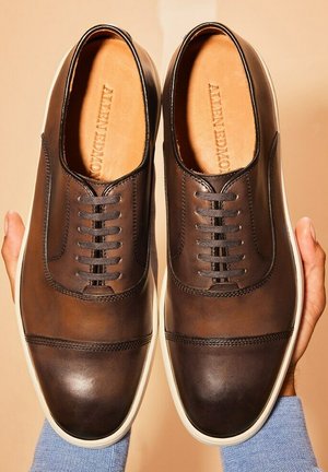 Bruine leren schoenen met een ronde neus, voorzien van een 5-oog veterontwerp, witte rubberen zool en subtiele stiksels.