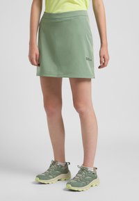Groene sportrok met een zachte textuur en een comfortabele tailleband, gecombineerd met grijs-groene wandelschoenen met gele accenten.
