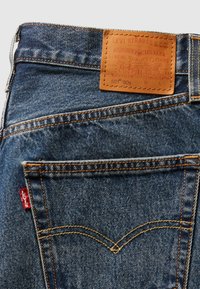 Τζιν παντελόνια από τζιν με καφέ δερμάτινο ένθετο με την επιγραφή «Levi Strauss & Co.», που διαθέτουν πορτοκαλί ραφές και μια κόκκινη ετικέτα στην πίσω τσέπη.