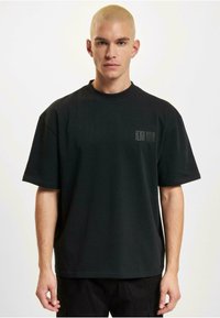 Black short-sleeve t-shirt made of cotton with a relaxed fit. Features a small printed logo on the front in a contrasting color.
