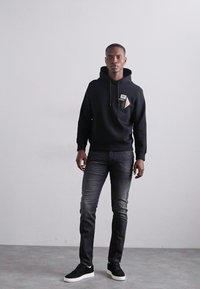 Svart hoodie med känguruficka och snören, tillsammans med mörkgrå slim-fit jeans och svarta sneakers med vit sula.