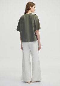 Olivově zelený oversize top s krátkými rukávy a texturovanými detaily, spárován s bílými kalhotami s širokými nohavicemi. Jednoduchý a moderní design.
