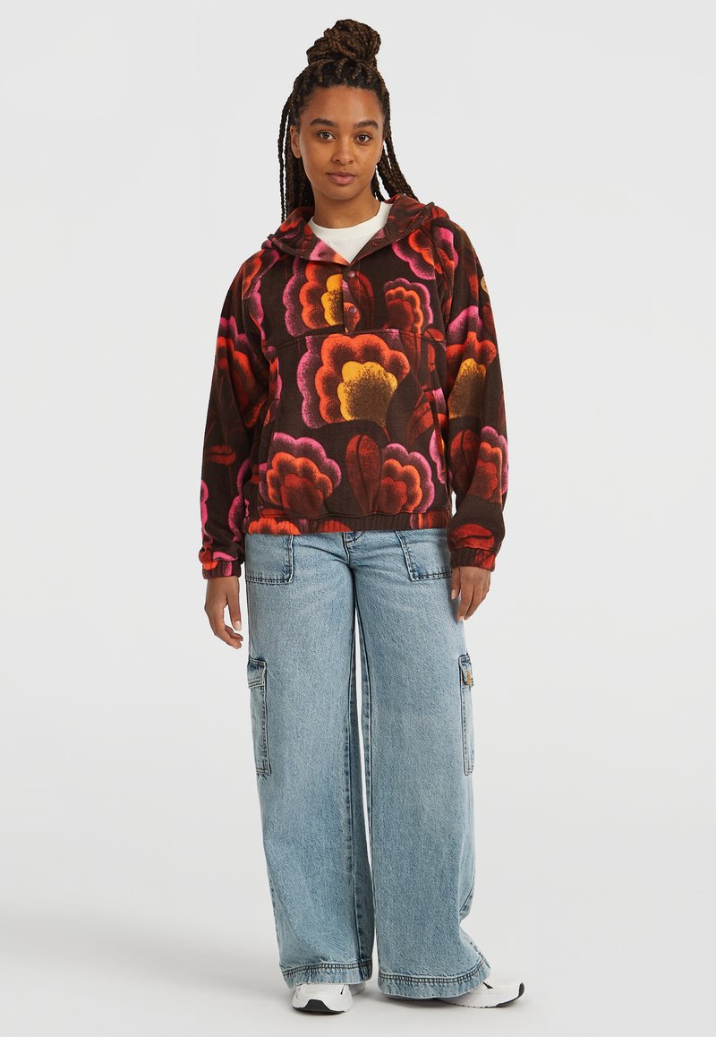 Brauner Fleece-Hoodie mit großen rot-rosa Blumenmustern, elastischen Bündchen und einer Fronttasche, kombiniert mit lockeren, hellblauen Denim-Cargo-Hosen.