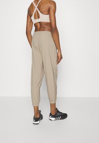 Beige Jogginghosen mit elastischen Bündchen, kombiniert mit einem hellbraunen Sport-BH mit Rautenrücken-Design und schwarzen Sportschuhen.