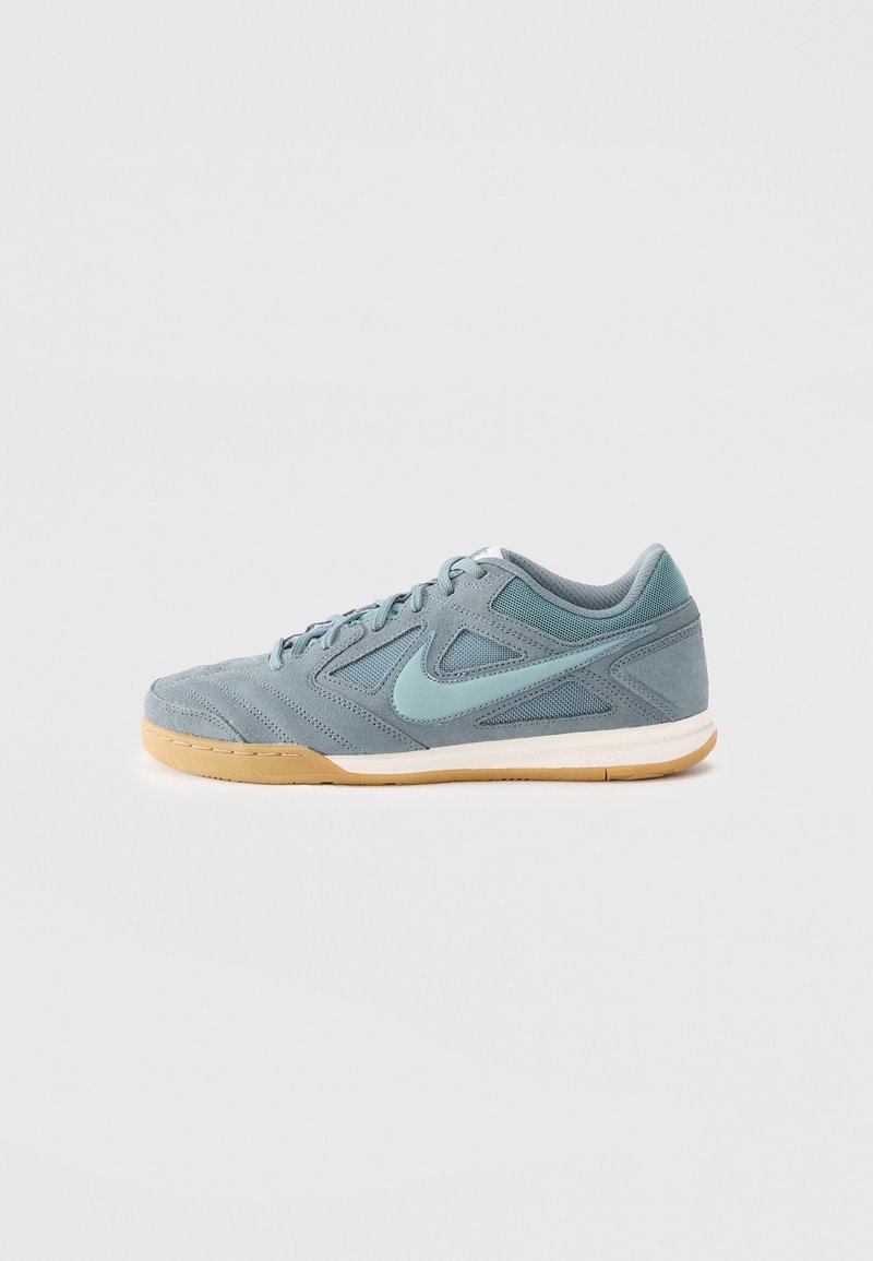 Chaussure de sport basse pour homme en suède gris et mesh, avec un swoosh Nike bleu clair et une semelle en gomme sur fond blanc.