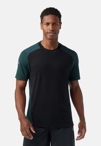 Svart tränings t-shirt med gröna strukturerade axelpaneler, korta ärmar och rundad halsringning. Tillverkad av lätt och andningsbart material.