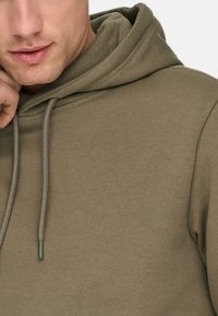 Hoodie vert olive avec cordon de serrage, en tissu doux, doté d'une poche kangourou et de poignets côtelés. Texture lisse, design décontracté.