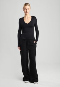 Black long-sleeve top with a V-neck, paired with wide black trousers featuring a drawstring waist and side pockets. Smooth fabric texture.