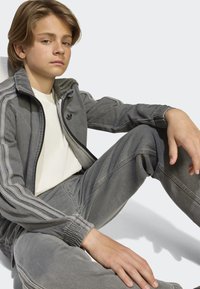 Gray Adidas track jacket with zip, ribbed cuffs, and logo. Paired with matching gray sweatpants, both in soft fabric and relaxed fit.