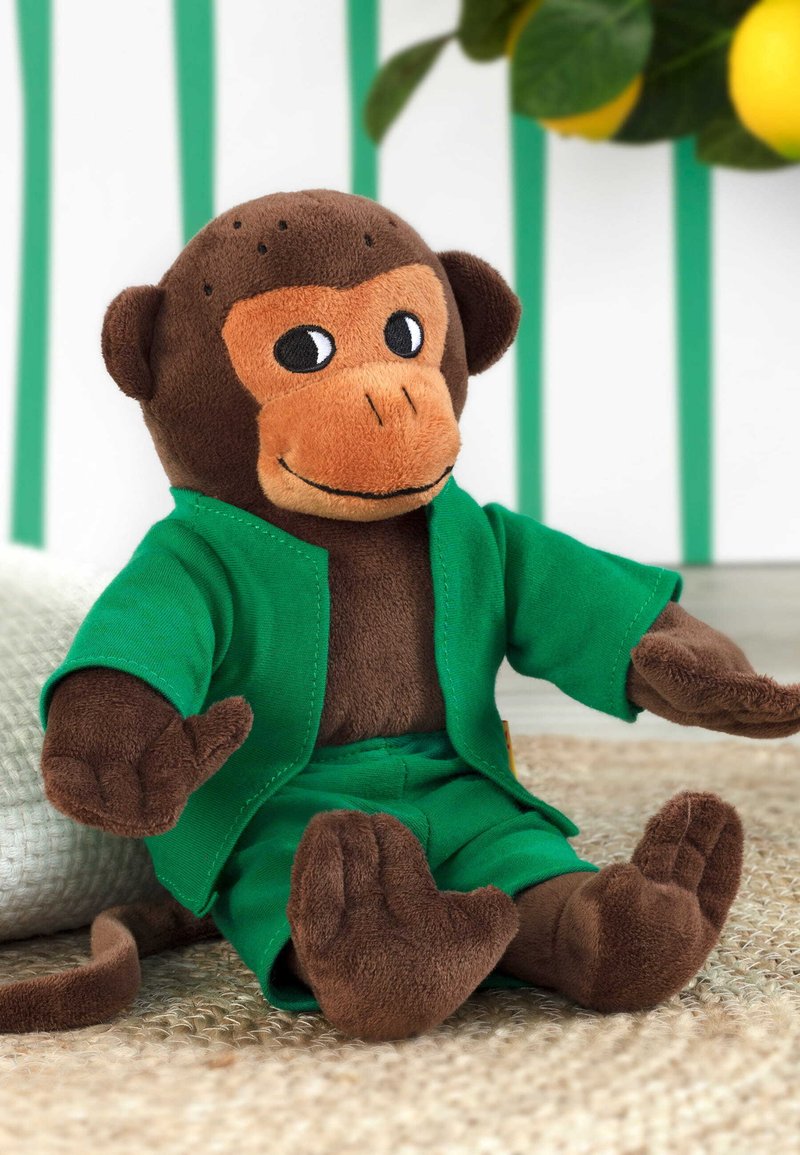 Bruine pluche aap speelgoed in een groene jas en broek, met een glimlachend gezicht en gedetailleerde gelaatskenmerken, zittend op een gestructureerd oppervlak.