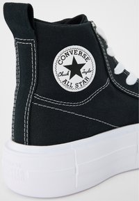 Svart lærkanvas høye sneakers med hvite snøringer, hvit gummisåle og rundt logo på siden. Har kontrasterende hvite søm detaljer.