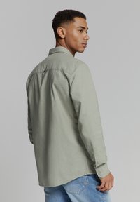 Lichtgroen overhemd met lange mouwen, gemaakt van zachte stof, met een klassieke kraag, knoopmanchetten en een rugplooi detail. Draagt bij blauwe jeans.