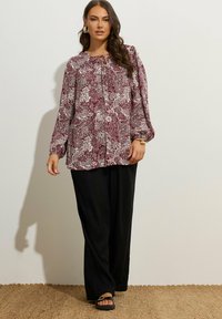 Blusa a maniche lunghe con un motivo paisley floreale in bordeaux e crema, con scollo arr gathered e chiusura a bottoni, abbinata a pantaloni larghi neri.