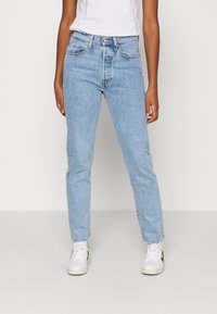 Jeans de mezclilla azul claro con un diseño de pierna recta, bolsillos delanteros y cintura alta. Llevados con zapatillas blancas.