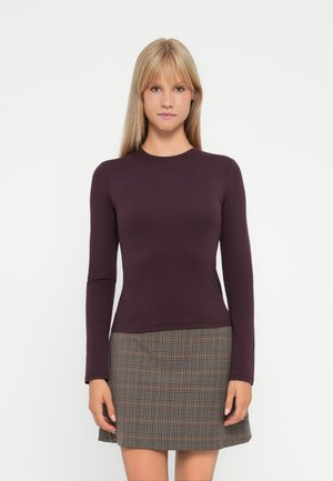 Haut à manches longues en violet profond, au design ajusté. Associé à une jupe à carreaux dans des tons atténués, présentant une forme en A et un tissu texturé.