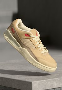 Baskets beiges en suede et en mesh, avec des accents rouges, un design à lacets et une semelle en caoutchouc texturé. Style minimaliste.