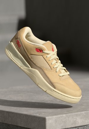 Beige sportcipő, velúr és hálós anyagból készült, piros akcentusokkal, fűzős kialakítással és textúrált gumitalppal. Minimalista stílus.