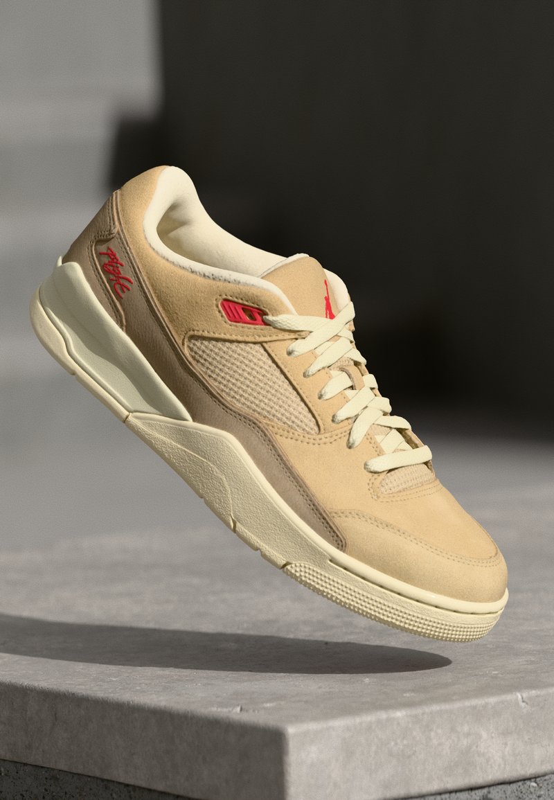 Baskets beiges en suede et en mesh, avec des accents rouges, un design à lacets et une semelle en caoutchouc texturé. Style minimaliste.